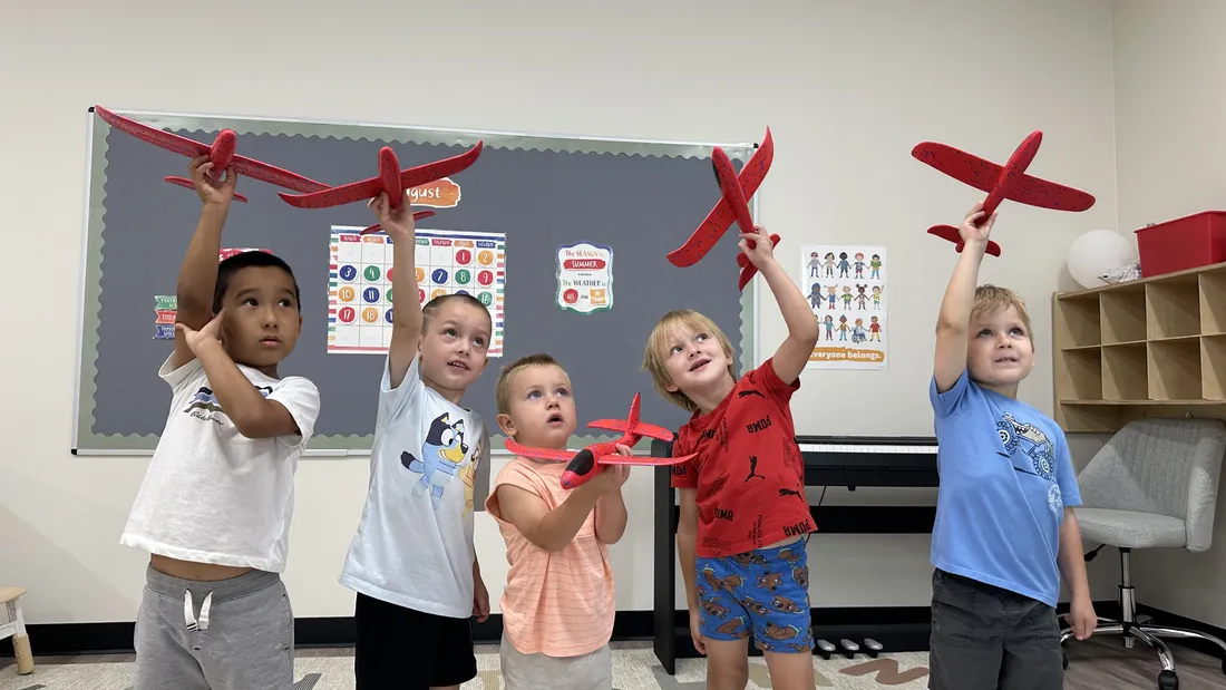 Children proudly holding red model airplanes during a classroom activity