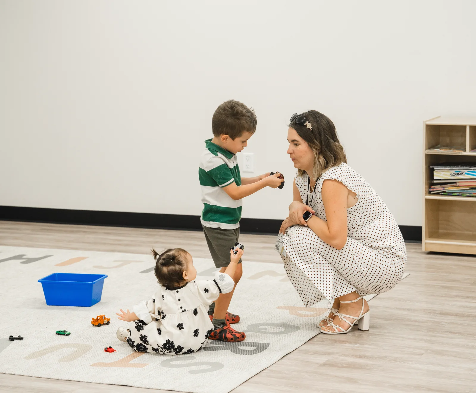 An educator engaging with two young children at their level in a bright classroom
